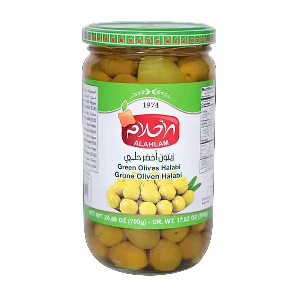 A glass jar of Alahlam Green Olives Halabi against a solid black background. The jar has a green and white label with the red Alahlam logo, and the green-lidded jar is filled with yellow-green olives.